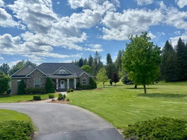 Charming home with landscaped lawn under a blue sky and scattered clouds, surrounded by trees.