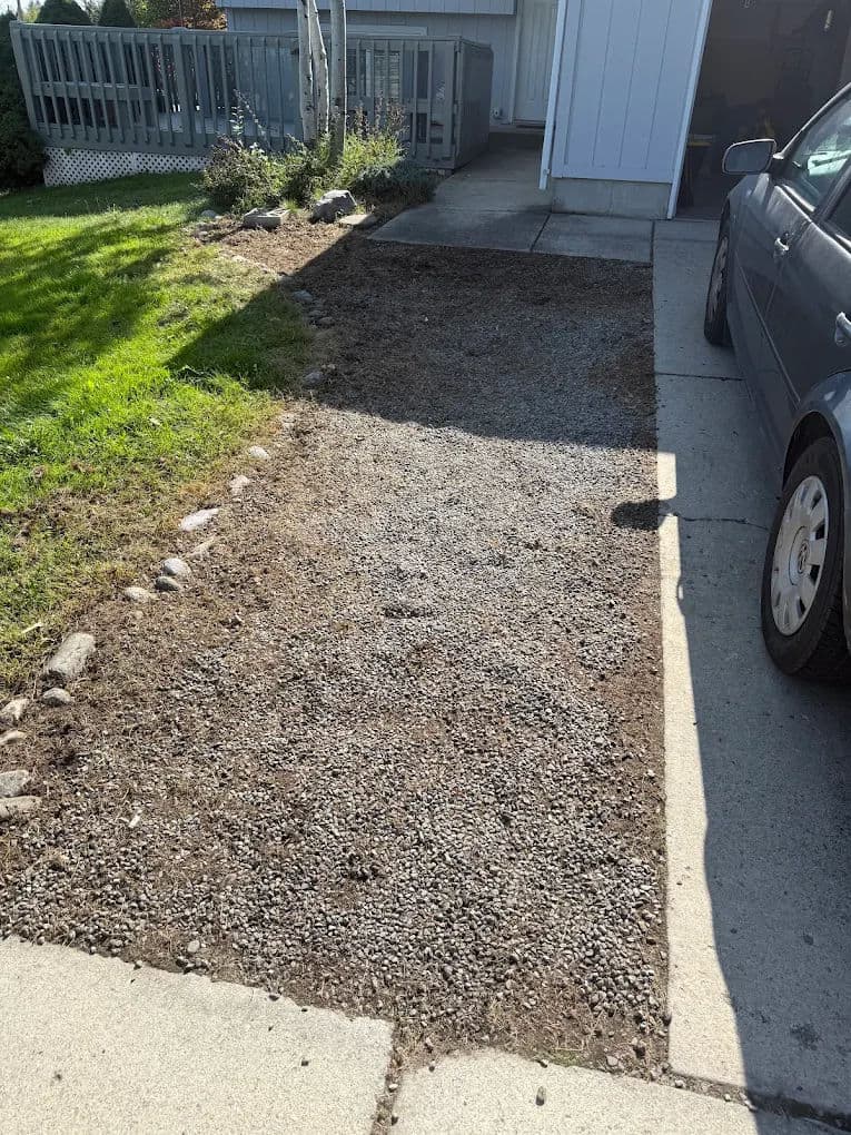 Gravel driveway extension with freshly laid stones and grass border next to a parked car.