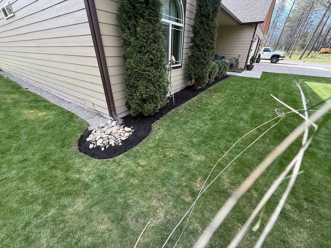 Lush green lawn beside home with neatly landscaped flowerbed and gravel accents.